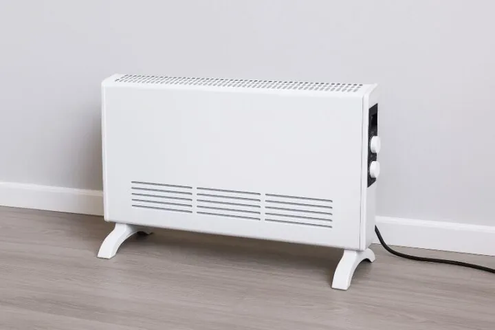 Slanke witte elektrische convectorheater op laminaatvloer, ideaal voor compacte ruimtes en energiezuinige verwarming.